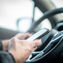 Person mit Handy am Lenkrad
